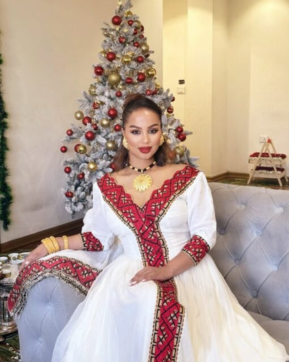 Woman in a white and red embroidered dress sitting in front of a decorated Christmas tree.