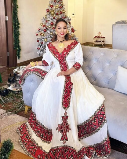 Woman in a white and red traditional outfit sitting on a couch with a decorated Christmas tree in the background.